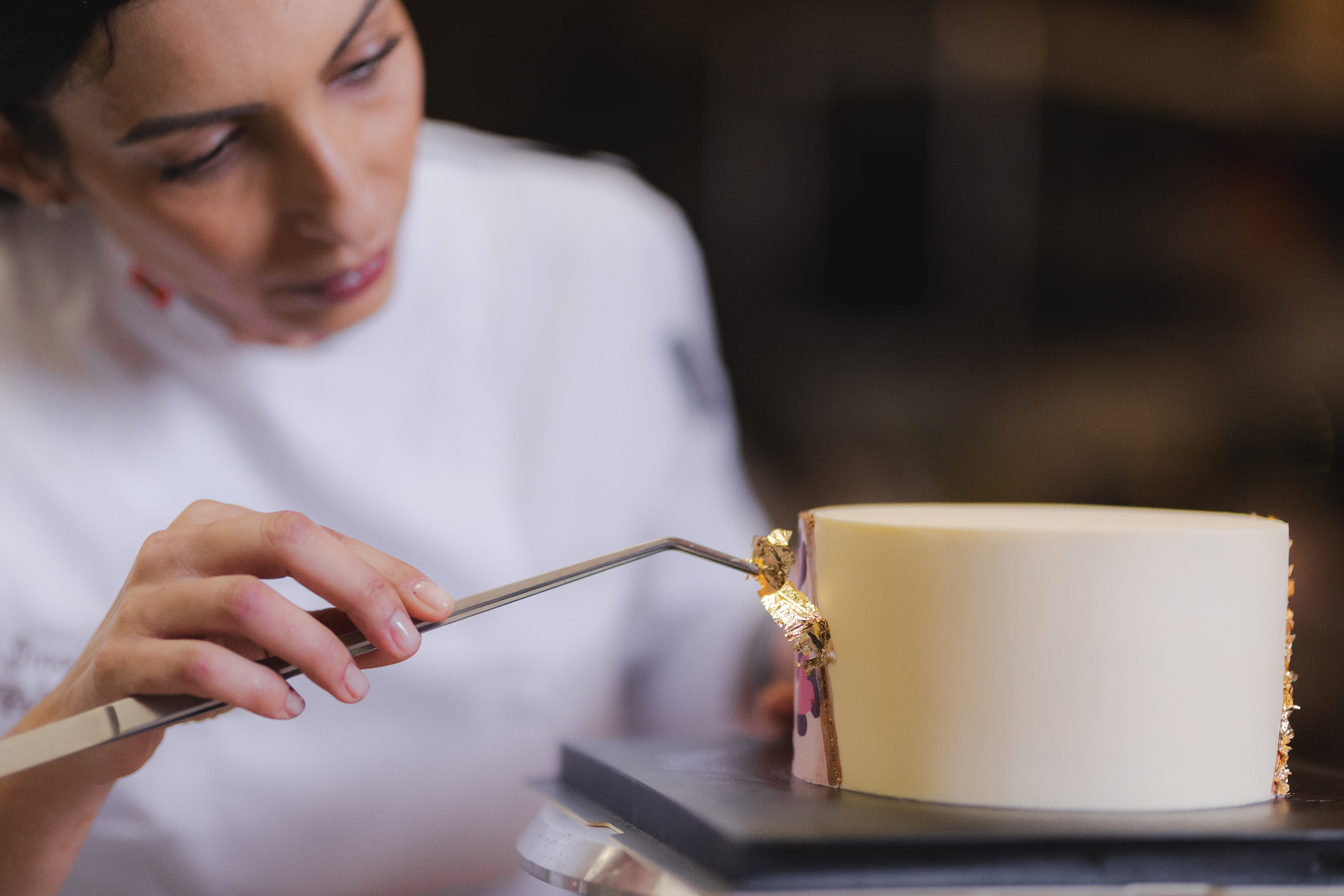 Imane, chef pâtissière My Bento Cake à Montpellier, posant une feuille d'or sur un gâteau
